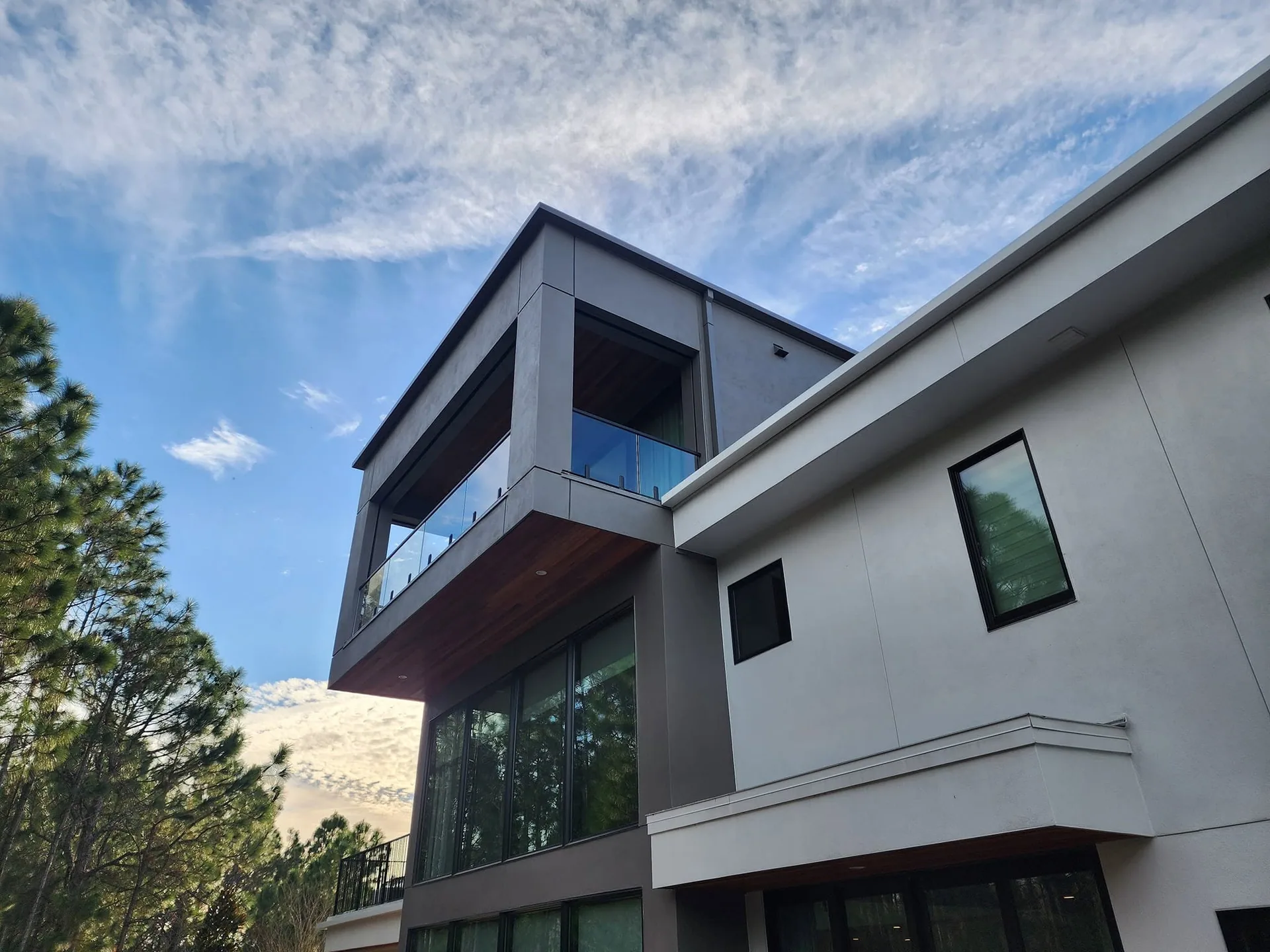 Low angle modern gray stucco cantilevered balcony glass railing wood soffit sanf